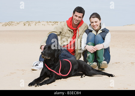 Couple sitting on beach with pet dog Stock Photo