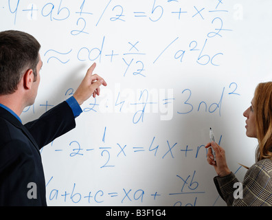 Male and Female Looking at Calculations and Formula on a Whiteboard Stock Photo