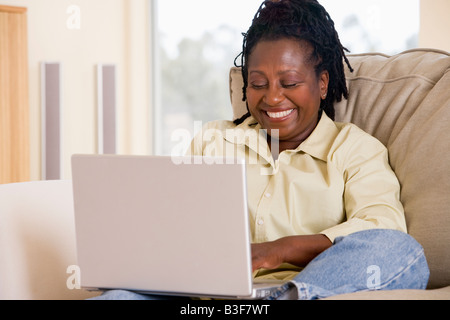 Woman in living room using laptop and smiling Stock Photo