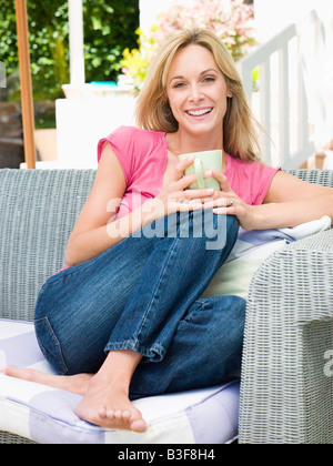 Woman sitting outdoors on patio with coffee smiling Stock Photo