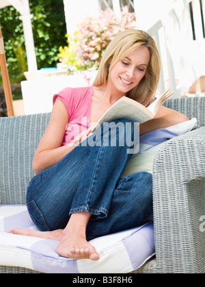 Woman sitting outdoors on patio with book smiling Stock Photo