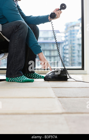 Man dialing phone at home, low section, side view Stock Photo