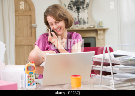 Mother and baby in home office with laptop and telephone Stock Photo