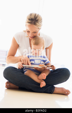 Mother and baby indoors reading book and smiling Stock Photo