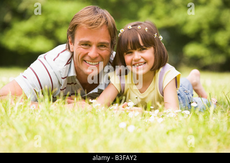 Father and daughter lying outdoors with flowers smiling Stock Photo
