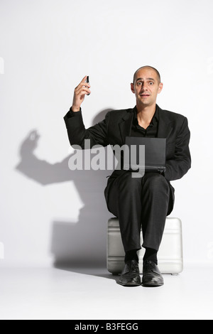 Man in a busines suit sat on a brief case lap top on knee holding a telephone Stock Photo