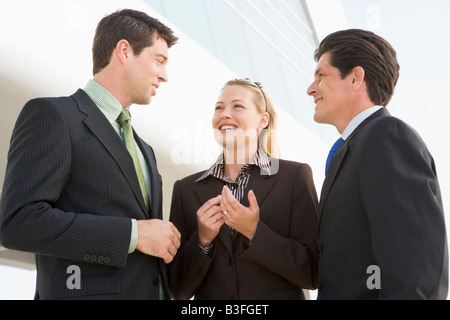 Three businesspeople standing outdoors by building talking and smiling Stock Photo