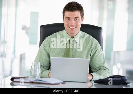 Businessman sitting in office with personal organizer using laptop smiling Stock Photo