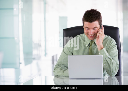 Businessman sitting in office using cellular phone and laptop Stock Photo