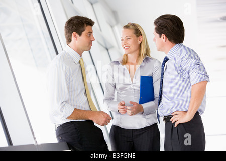 Three businesspeople standing in corridor talking and smiling Stock Photo