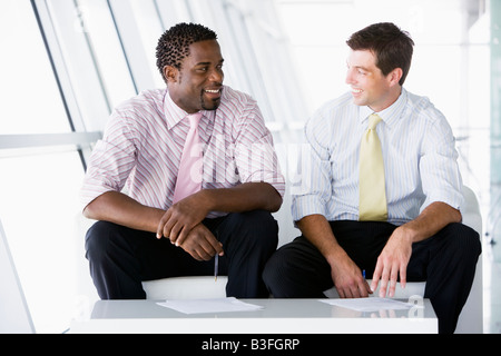 Two businessmen sitting in office lobby talking and smiling Stock Photo