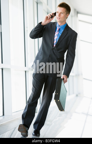 Businessman walking in corridor using cellular phone Stock Photo