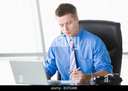 Businessman sitting in office with laptop writing note Stock Photo