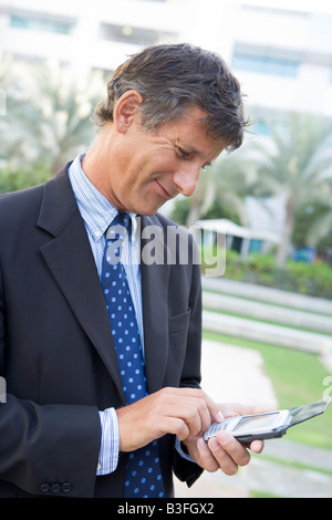 Businessman outdoors using personal digital assistant smiling Stock Photo