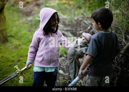 Girl aged five discusses an imaginary enemy with her six year old brother while handing over her toy doll Stock Photo