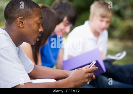 Four students outdoors studying with one checking cellular phone (depth of field) Stock Photo
