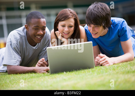 Three students lying outdoors on lawn with laptop Stock Photo