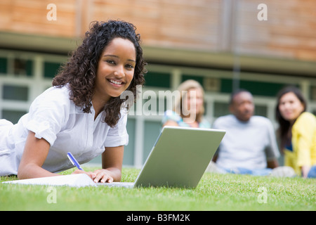 Student outdoors on lawn using laptop with other students in background (selective focus) Stock Photo
