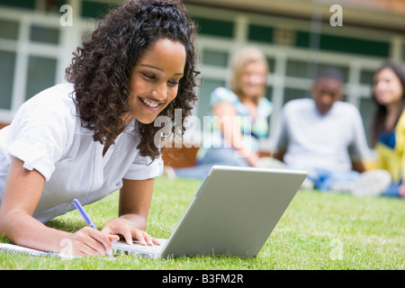 Student outdoors on lawn using laptop with other students in background (selective focus) Stock Photo