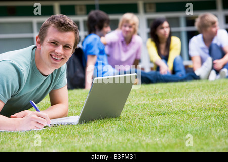 Student outdoors on lawn using laptop with other students in background (selective focus) Stock Photo