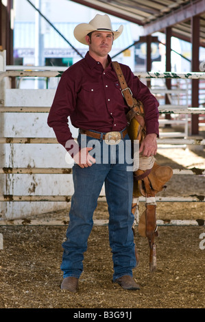 Idaho. A cowboy stands with his saddle in a corral at a rodeo. Stock Photo