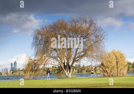 Two man walking and running in a city park with skyscrapers in the distance. Lake Monger Reserve, Perth, Western Australia Stock Photo