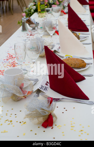 A decorated wedding table with red napkins, favours and confetti. Also place names on the table including one for the best man. Stock Photo