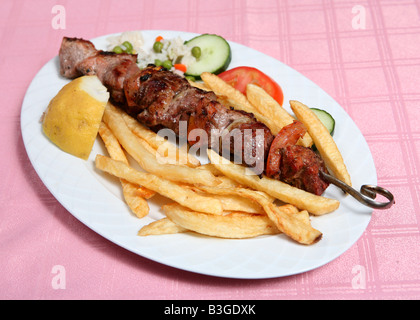 A pork souvlaki or kebab served on the skewer with fried potato chips rice and vegetables Souvlaki is a Greek taverna standard Stock Photo
