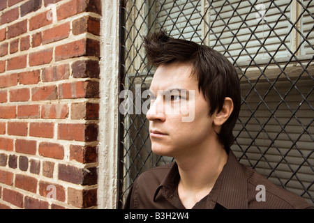 Asian man leaning against window near brick wall Stock Photo