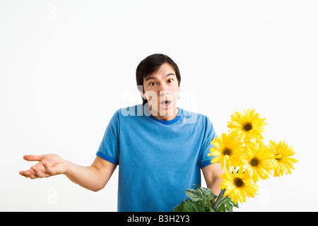 Asian young man holding bouquet of yellow gerber daisies shrugging Stock Photo