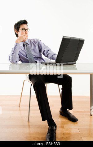 Asian businessman sitting at desk working on laptop computer Stock Photo