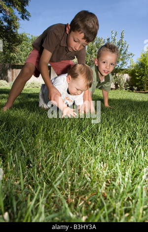 six year old brother and four year old brother help seven month old baby crawl outside in the grass Stock Photo