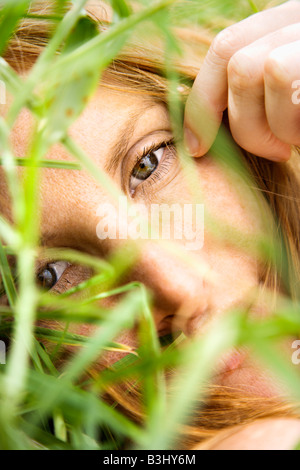 Close up portrait of pretty redhead lying in grass looking at viewer Stock Photo