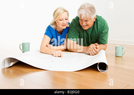 Middle aged couple lying on floor looking at and discussing architectural blueprints together Stock Photo