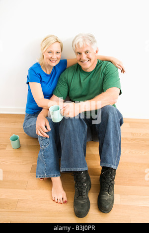 Middle aged couple sitting on floor together drinking coffee Stock Photo