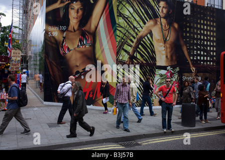 Pedestrian shoppers pass-by a giant summer fashion hoarding for H&M in London's Oxford Street Stock Photo