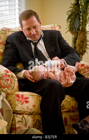 Wearing a look of committed concern an over 40 Irish American man bottle feeds his infant daughter MODEL RELEASE Stock Photo