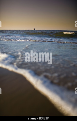 The Breakwater Lighthouse with waves crashing against the Delaware shoreline at Cape Henlopen State Park Stock Photo