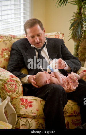 Wearing a look of committed concern an over 40 Irish American man bottle feeds his infant daughter MODEL RELEASE Stock Photo