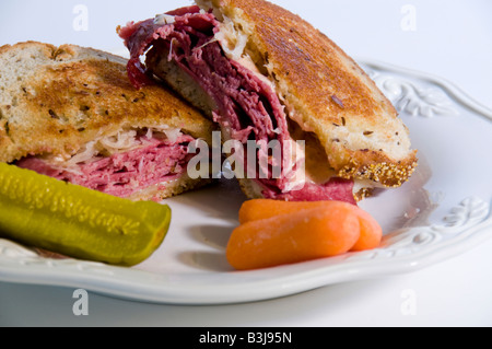 Reuben sandwich with a pickle and carrots on a while plate. Stock Photo