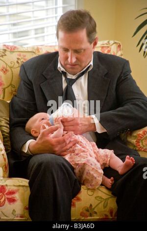 Wearing a look of committed concern an over 40 Irish American man bottle feeds his infant daughter MODEL RELEASE Stock Photo