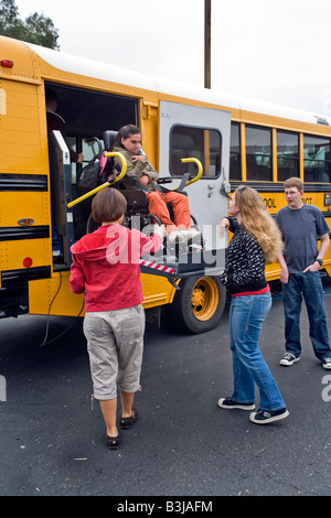 A wheelchair bound special needs student arrives at school via a handicapped lift on a modified school bus Teacher wears gloves Stock Photo