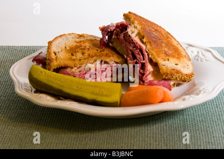 Rueben sandwich with a pickle and carrots on a white plate. Stock Photo