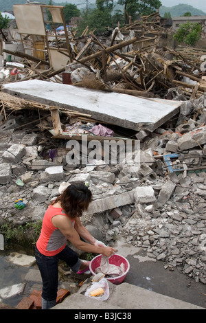 A survivor of earthquake in Sichuan on May 12 2008 washes clothes street gutter outside the ruins of her home. Stock Photo