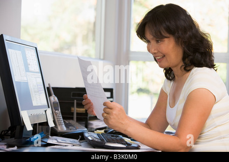 Woman in home office with computer and paperwork smiling Stock Photo