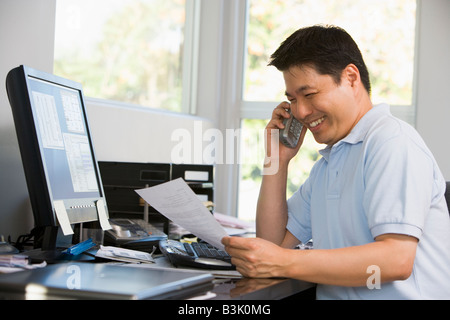 Man in home office with computer and paperwork on telephone smiling Stock Photo
