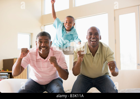 Two men and young boy in living room cheering and smiling Stock Photo