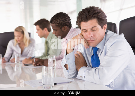 Four businesspeople in boardroom with one businessman sleeping Stock Photo