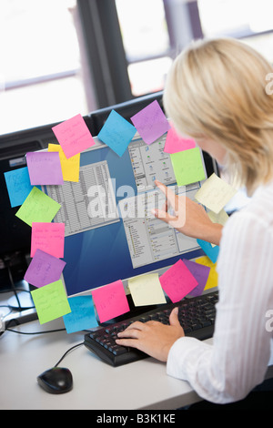 Businesswoman in office pointing at monitor with notes on it Stock Photo