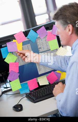 Businessman in office at monitor with notes on it Stock Photo